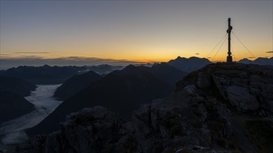 Sunrise with cross of the Thanell summit and Lechtal Alps with fog in the valley