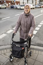 Senior citizen with rollator crosses a street in the city
