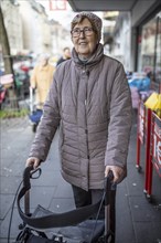 Senior citizen with rollator in a shopping street in front of One-Euro Shop