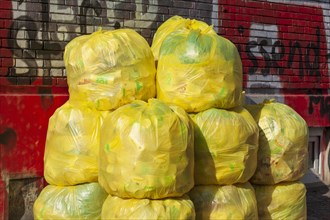 Stacked yellow bags for plastic waste in front of a house wall