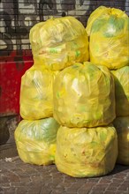 Stacked yellow bags for plastic waste in front of a house wall