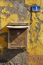 Wooden mailbox with house number one on house wall with flaking paint