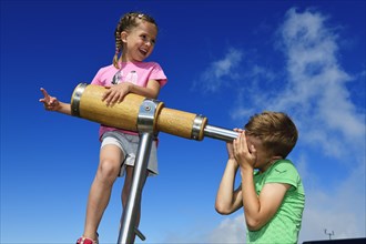 Girl and boy looking through a wooden telescope