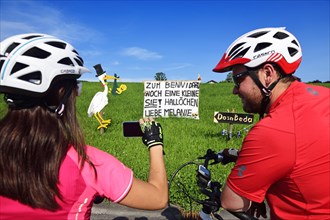 Cyclists photographing Rattling stork and banner as a welcome for a newborn child