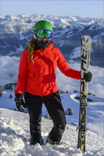 Skier with ski helmet and ski stands in front of mountain panorama