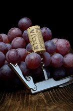 Corkscrew with cork and red grapes
