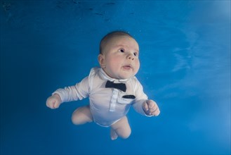 Little boy in white suit and bow tie swimming underwater