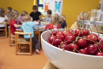 A bowl of cherries stands in the dining room in the kindergarten and children sit at the table to eat