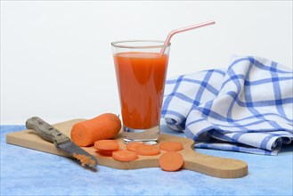 Carrot juice in glass and carrot slices on wooden board