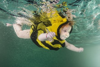 Redhead little girl in bee costume swim underwater in a pool