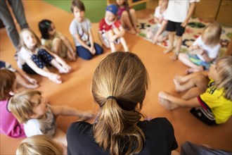 Educator sits with children in the kindergarten in a circle on the floor