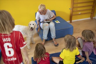 Children are read to in the kindergarten by a teacher in the presence of a dog