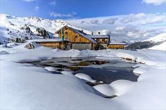 Snowy Lizumer Hut with small mountain lake in winter