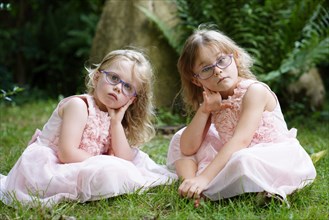 Two sisters in pink dress sitting in the garden (6 years old