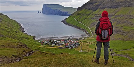 A hiker looks at the small village Tjornuvik and the Atlantic Ocean