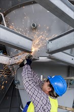 Construction worker processes a steel beam with an angle grinder on a large construction site