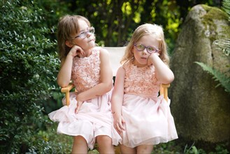 Portrait of two sisters sitting together on a garden chair (6 years old