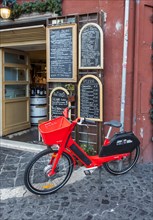 Red JUMP electric rental bike outside Italian restaurant with handwritten blackboard menu