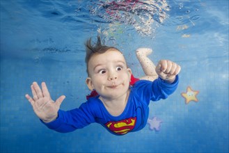 Little boy in a superman costume dives underwater in the pool