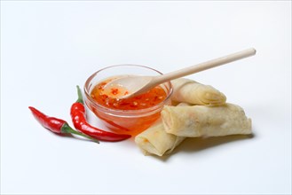 Chilli sauce in small bowls with chilli peppers and mini spring rolls
