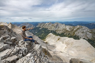 Hiker sitting at the summit of the Birkkarspitze pointing into the distance