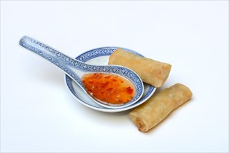 Chilli sauce in Asian spoon and mini spring rolls