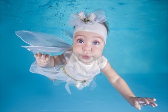 Little girl in fairy costume dives underwater in a swimming pool