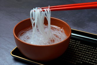 Asian glass noodles on chopsticks over bowl