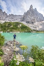 Young man hiker at the turquoise-green Sorapis lake with flowers