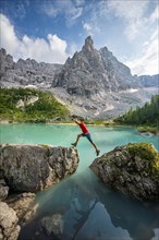 Hiker jumps from stone to stone at the turquoise green Sorapis lake