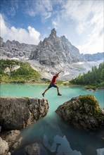 Hiker jumps from stone to stone at the turquoise-green Sorapis lake