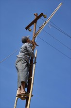 Young man in Longyi stands on ladder and repairs power line