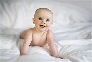 Baby boy on white bed sheets smiling