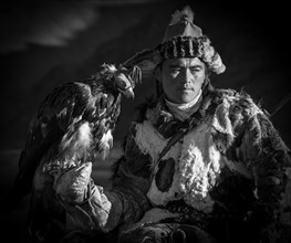 Mongolian eagle hunter poses with eagle with hood