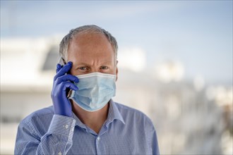 Man with protective mask and blue latex gloves while using mobile phone
