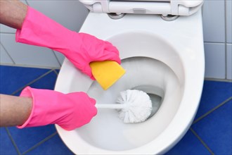 Person with rubber gloves cleans toilet with brush