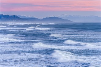 Leaking waves of the ocean under a pink evening sky with mountain silhouette, Punakaiki