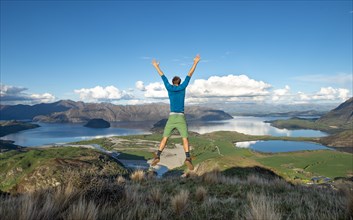 Hiker jumps in the air, view of Wanaka Lake and mountains