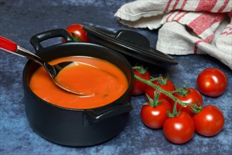 Tomato soup in pot with tablespoon, tomatoes