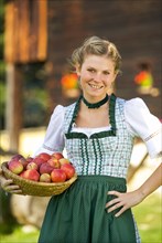 Young woman in dirndl wearing a basket of apples, 19 years