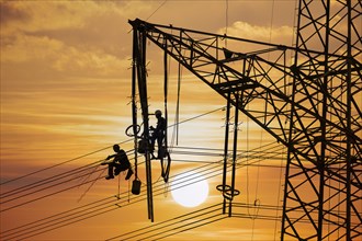 High voltage fitters working on the high voltage pylon at sunset, Baden-Wuerttemberg
