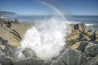 Blowhole with rainbow, splashing surf hole in the rock formations of Pancake Rocks