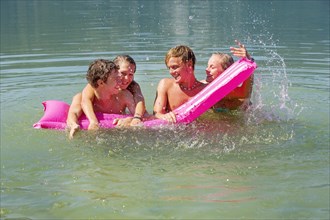 Four teenagers on an air mattress in water have fun bathing, 18 years