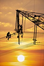 High voltage fitters working on the high voltage pylon at sunset, Baden-Wuerttemberg