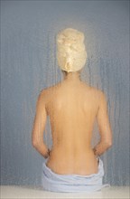 Woman sitting in a steam bath behind glass pane with drops of water, 24 years