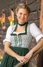 Young woman in dirndl standing in front of an old farmhouse, 19 years old