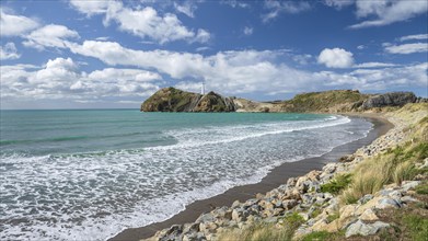 Beach with turquoise sea, in the back lighthouse of Castlepoint