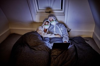 Couple in protective clothing in bed watching movies, Sylt
