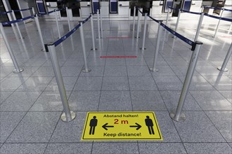 Sign with distance rule in front of the deserted baggage check, flight ban due to corona pandemic