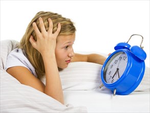 Girl in bed looks astonished at alarm clock